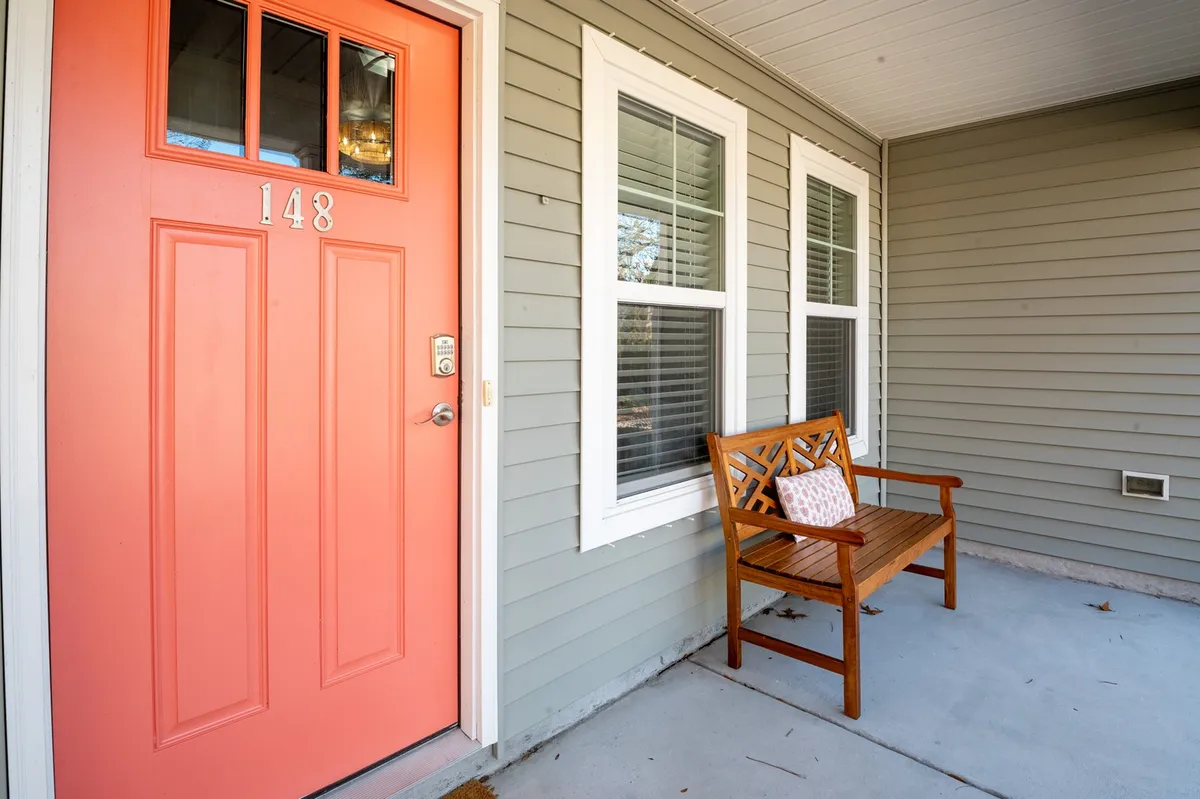 An inviting view of the entryway from inside, with the coral front door, a wooden bench with decorative pillow, and morning sunlight filtering through the space. The setting suggests easy, comfortable entry and a warm welcome.