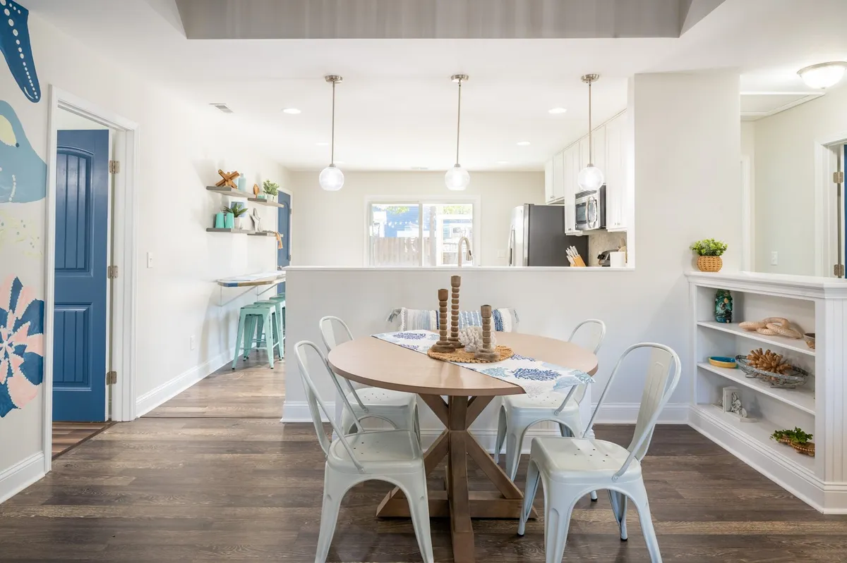 This image features a round wooden dining table surrounded by white metal chairs, accented by decorative shelves and a striking blue accent wall. The atmosphere is inviting and relaxed, suggesting a space ideal for group gatherings and family meals.