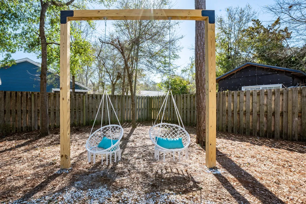 A cheerful, sunlit backyard view featuring hanging swings with colorful cushions set against natural surroundings. The scene evokes summer afternoons spent socializing, relaxing, or enjoying playful moments with loved ones.