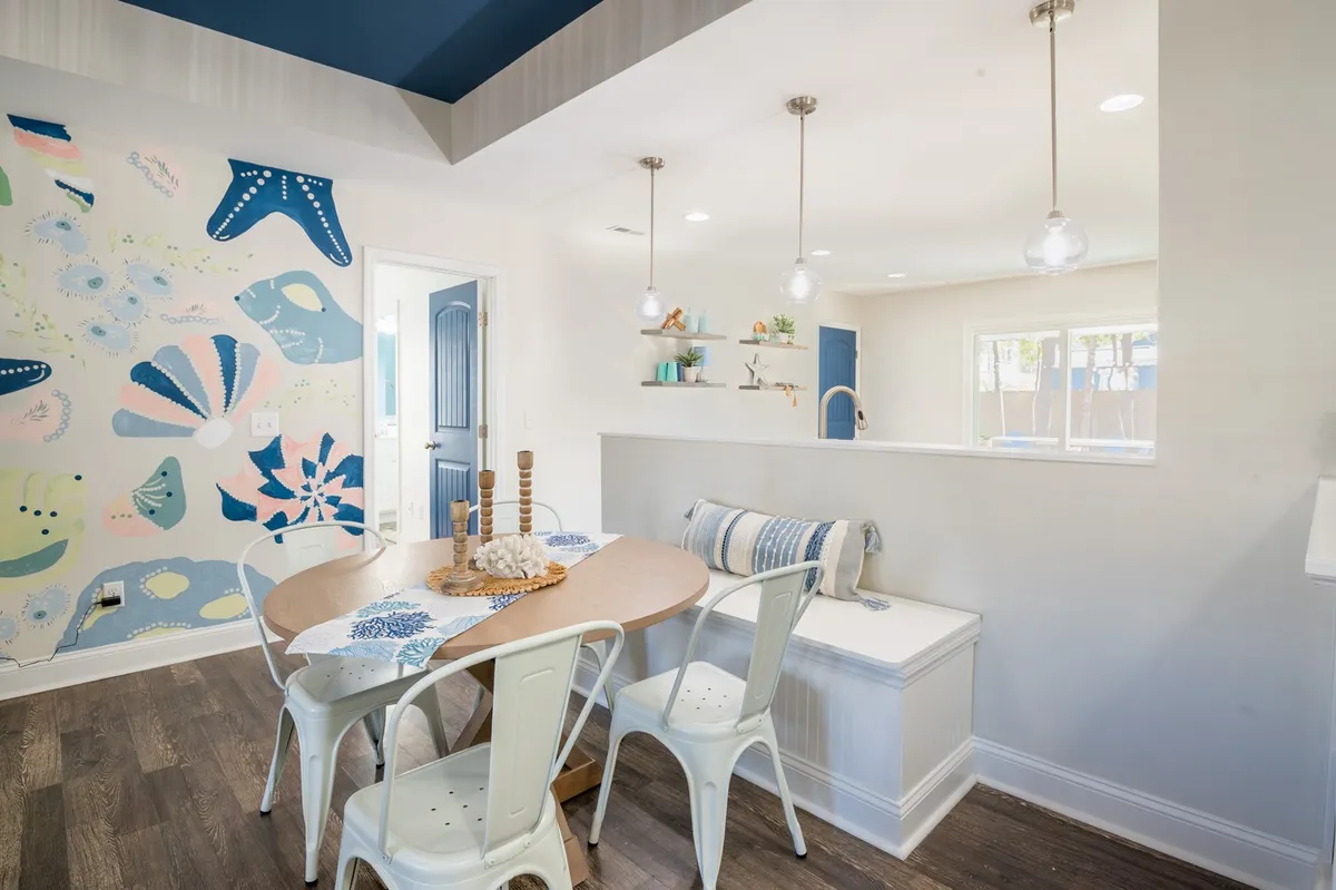 A cheerful dining area with a round wooden table and colorful mural, illuminated by pendant lights. The space feels vibrant yet relaxed, ideal for family meals or planning the day’s outings together.