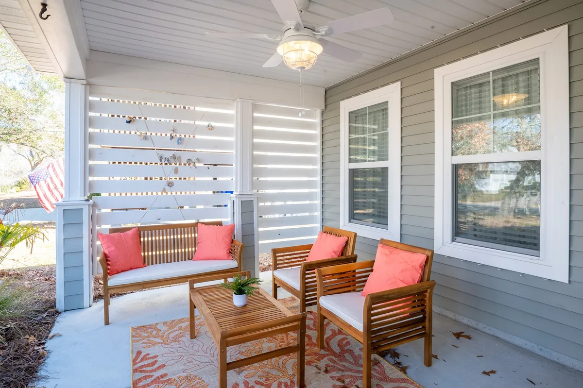 This image presents a comfortable screened porch with a seating area, decorative rug, ceiling fan, and lush greenery. The atmosphere is cozy and welcoming, perfect for morning coffee, al fresco dinners, or catching a game on the outdoor Smart TV.