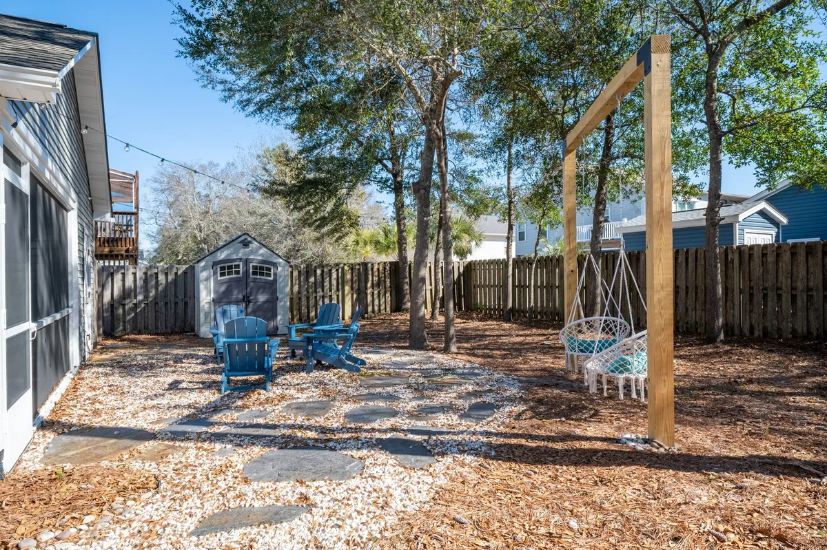 This exterior image features blue Adirondack chairs arranged around a manicured backyard, a whimsical hammock swing, and a garden shed. The tranquil setting invites relaxation and family gatherings in a private outdoor retreat.