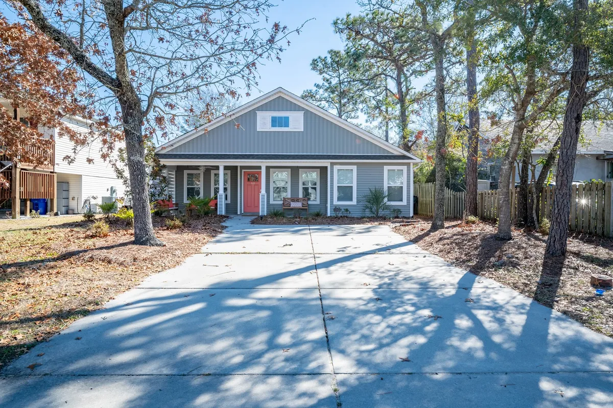 The exterior shot captures the front porch with cushioned seating, a bright door, landscaped yard, and driveway. It also subtly depicts the ease of access via the no-stair entry and shows ample parking space extending from the driveway, hinting at room for cars, boats, or trailers.