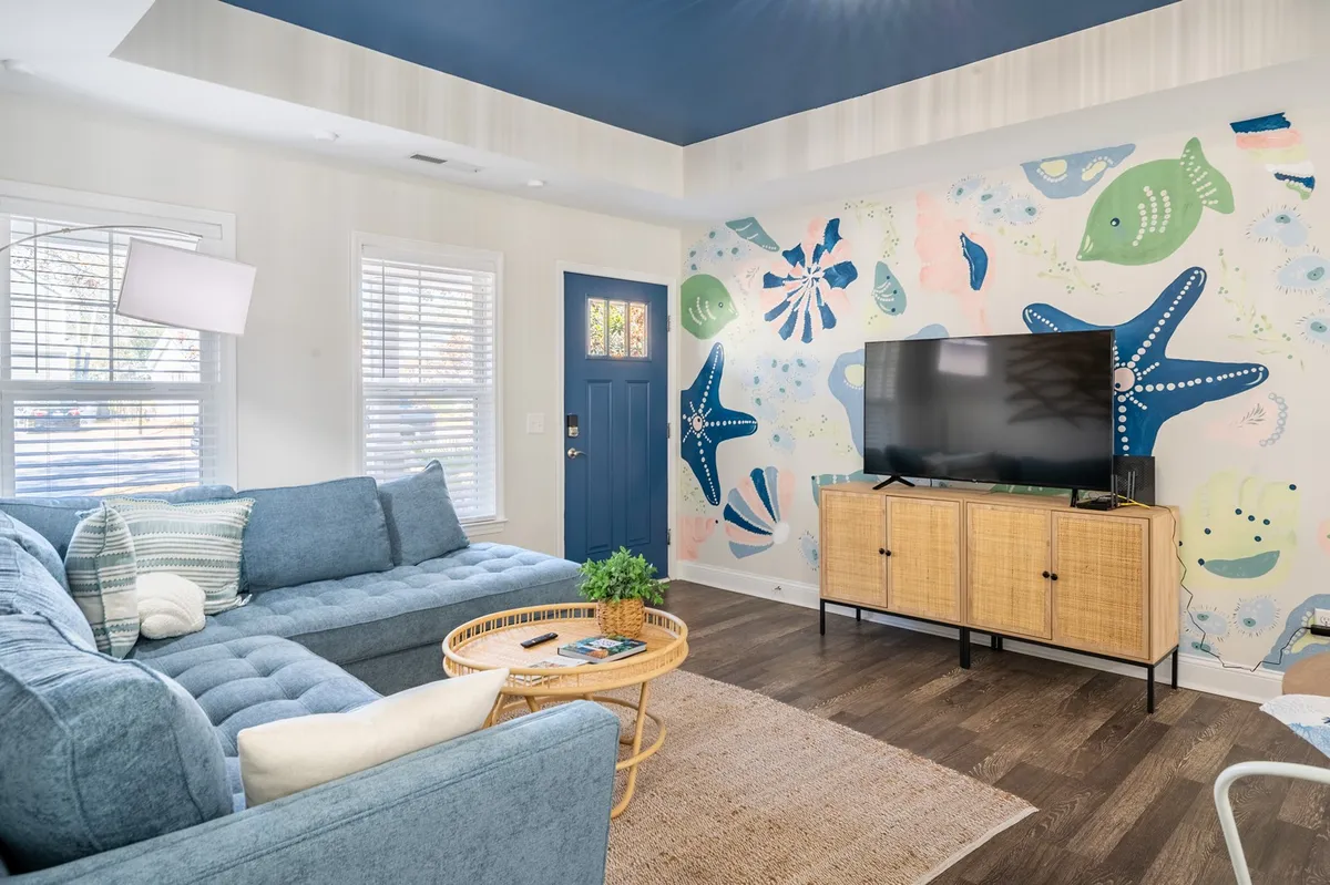 This image highlights a vibrant living room with a colorful mural wall as the backdrop to a blue sofa, complemented by a wooden TV cabinet. The setting feels lively and playful, ideal for family gatherings or relaxing evenings spent watching TV.
