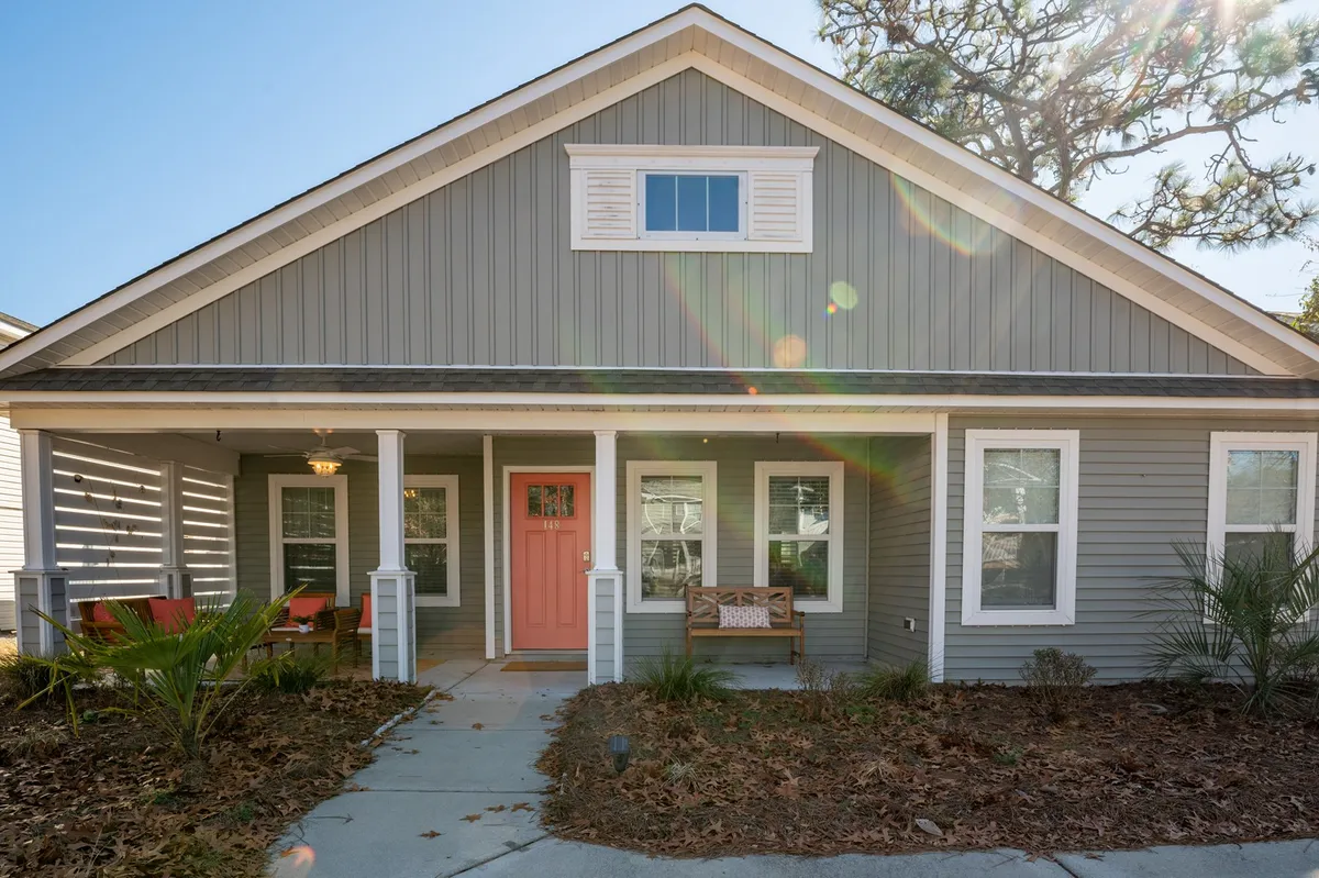 A welcoming exterior view of the home's front entry, featuring a charming porch with seating and tasteful landscaping. The scene is sunlit, highlighting the inviting atmosphere and the potential for relaxing social moments outdoors.