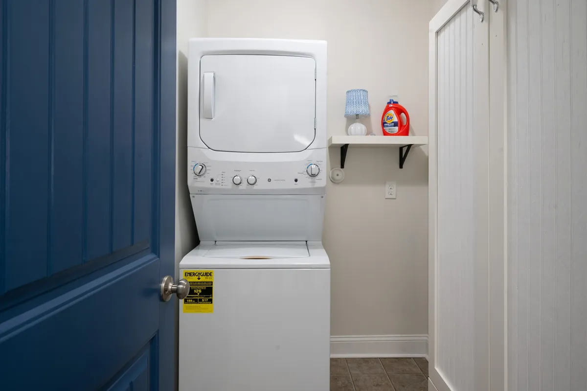 A functional laundry area featuring a washer and dryer unit, a shelf stocked with detergent, and a blue door. The space is clean, organized, and designed for convenience, reinforcing easy living for active guests.